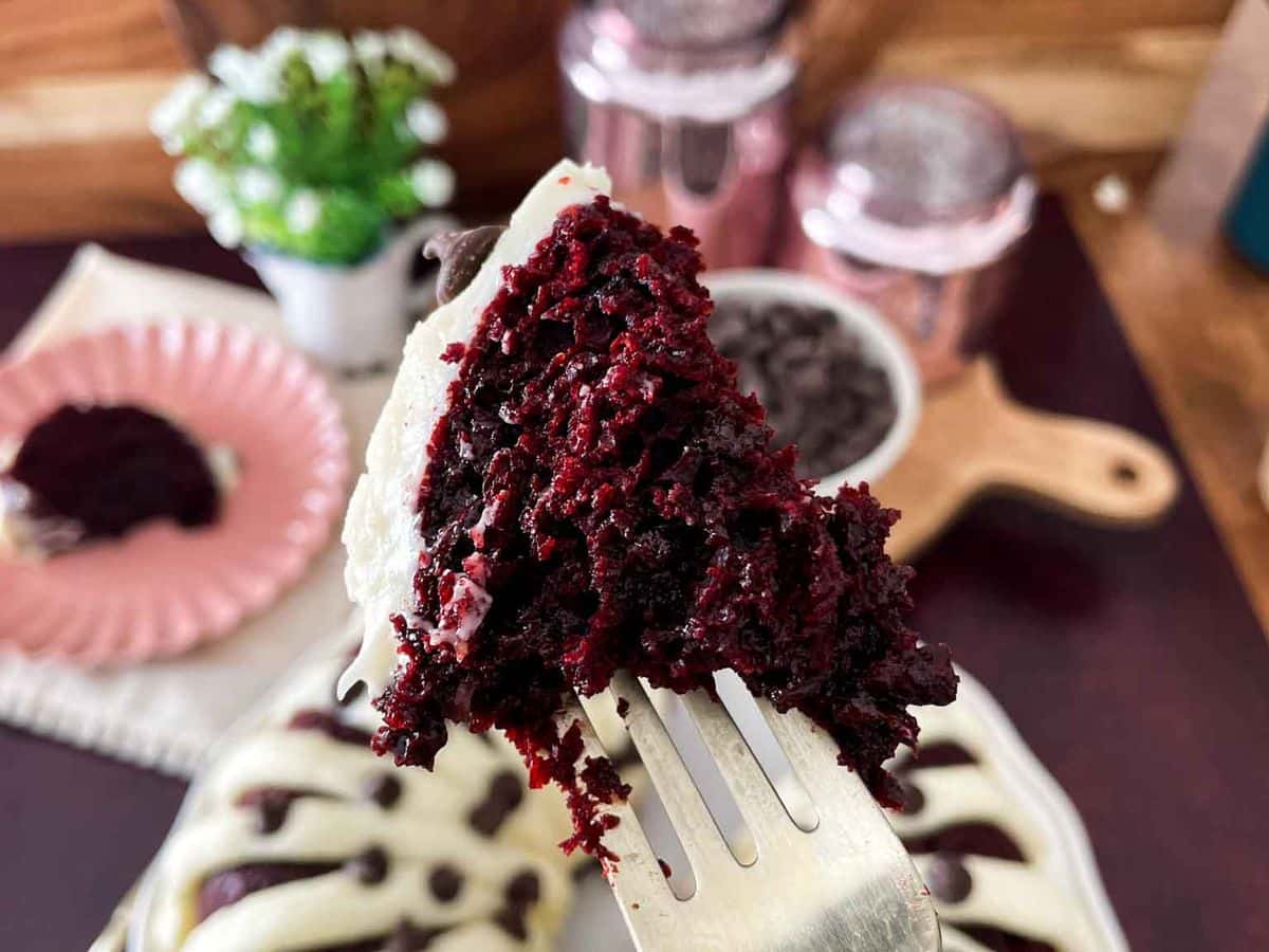 bite of red velvet cake on a fork with entire cake beneath it