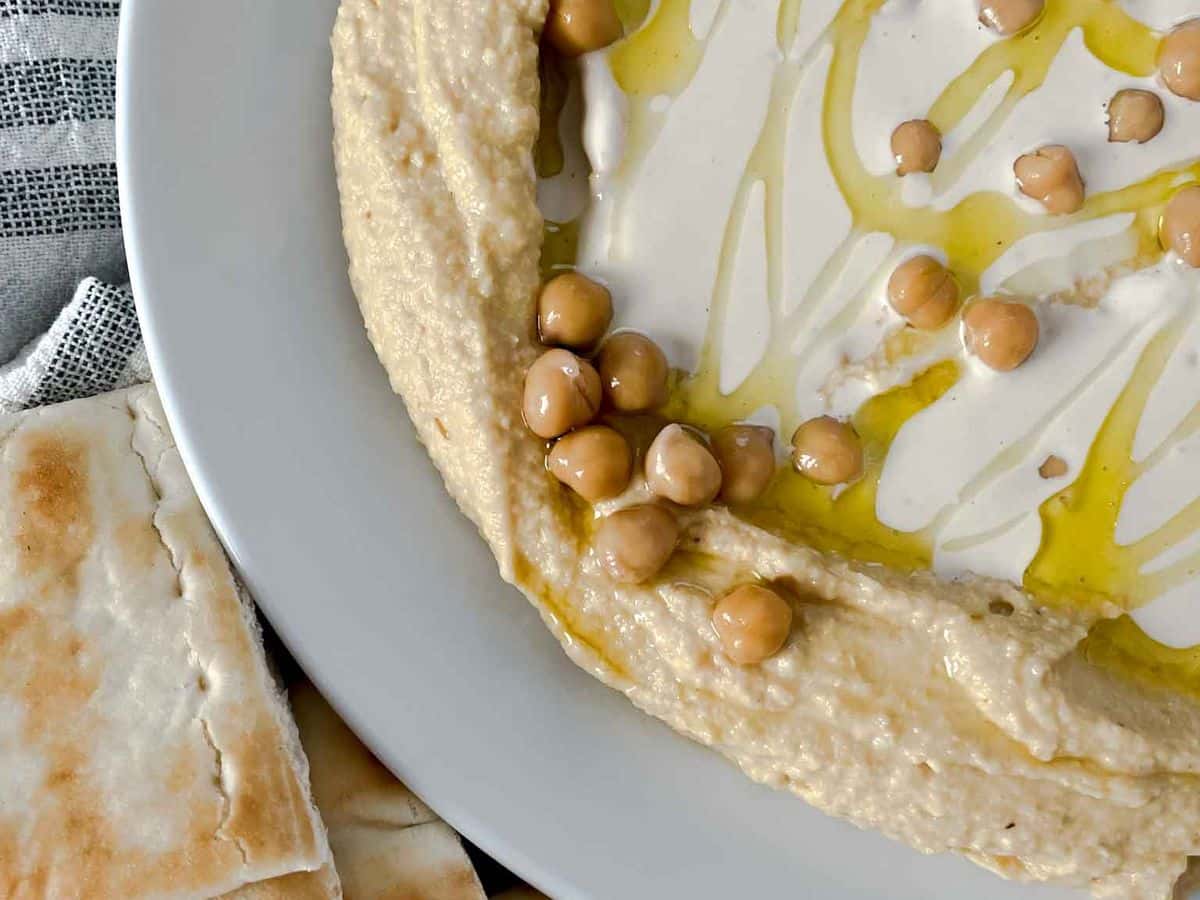a plate of homemade hummus with tahini sauce with pita bread on the side