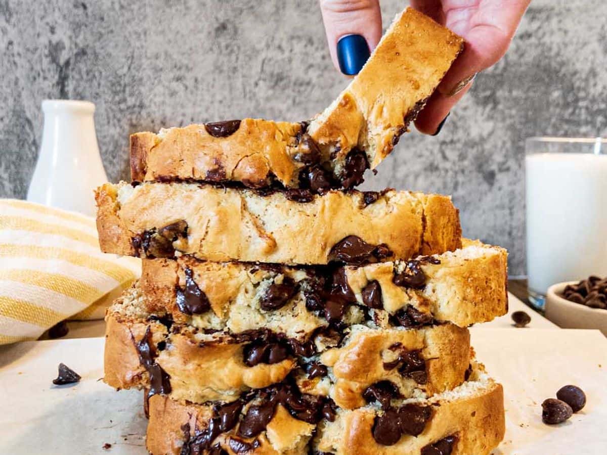 banana bread with chocolate chips, sliced and stacked with a hand pulling off the top slice