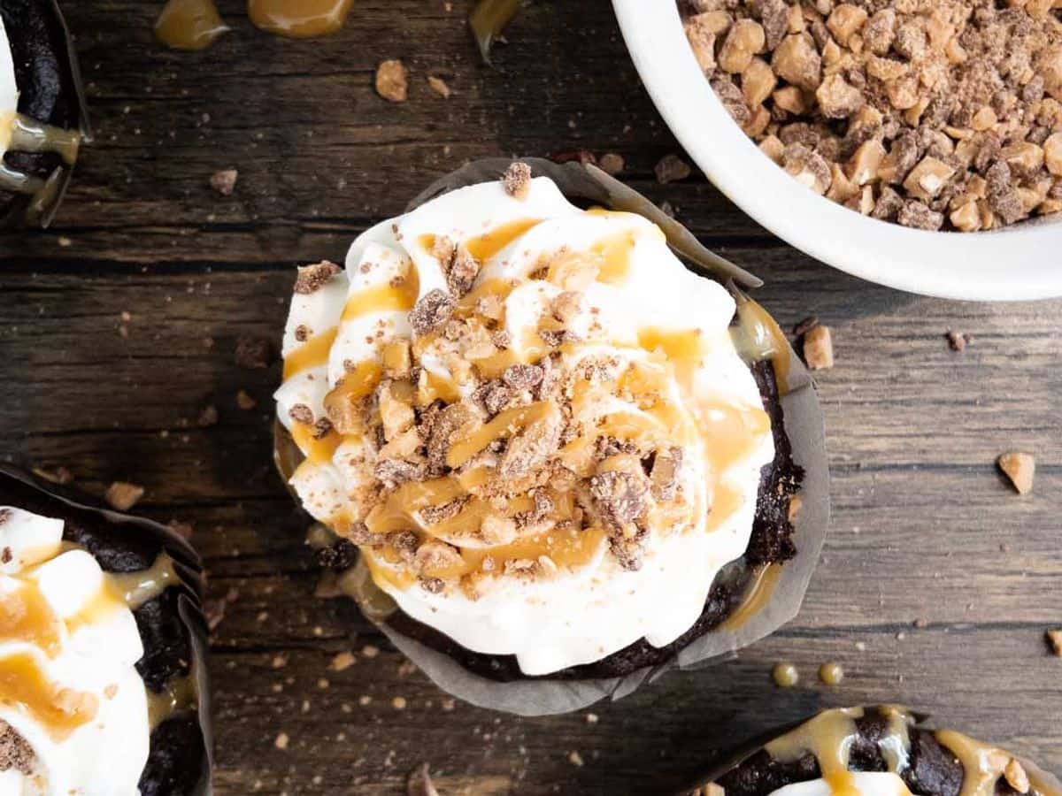 better than sex cupcakes topped with whipped cream, caramel sauce, and Heath bits, with bowl full of Heath bits to the side