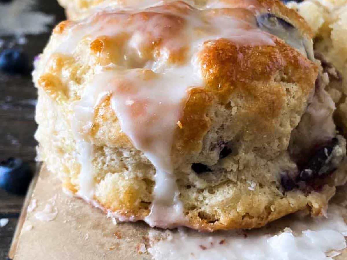boberry biscuits with blueberries and icing from the side on the back of a baking sheet with stick of butter in background