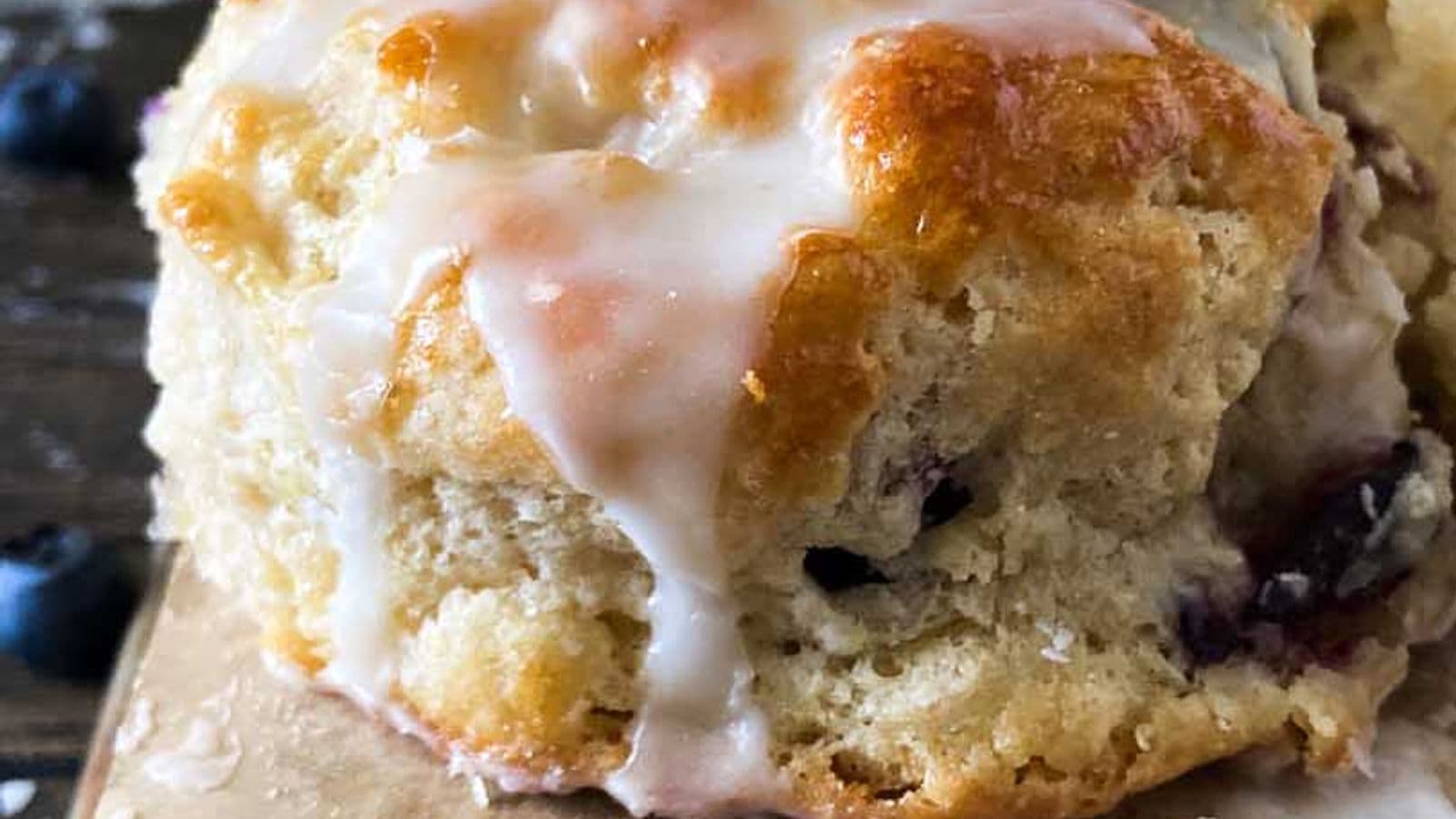 boberry biscuits with blueberries and icing from the side on the back of a baking sheet with stick of butter in background
