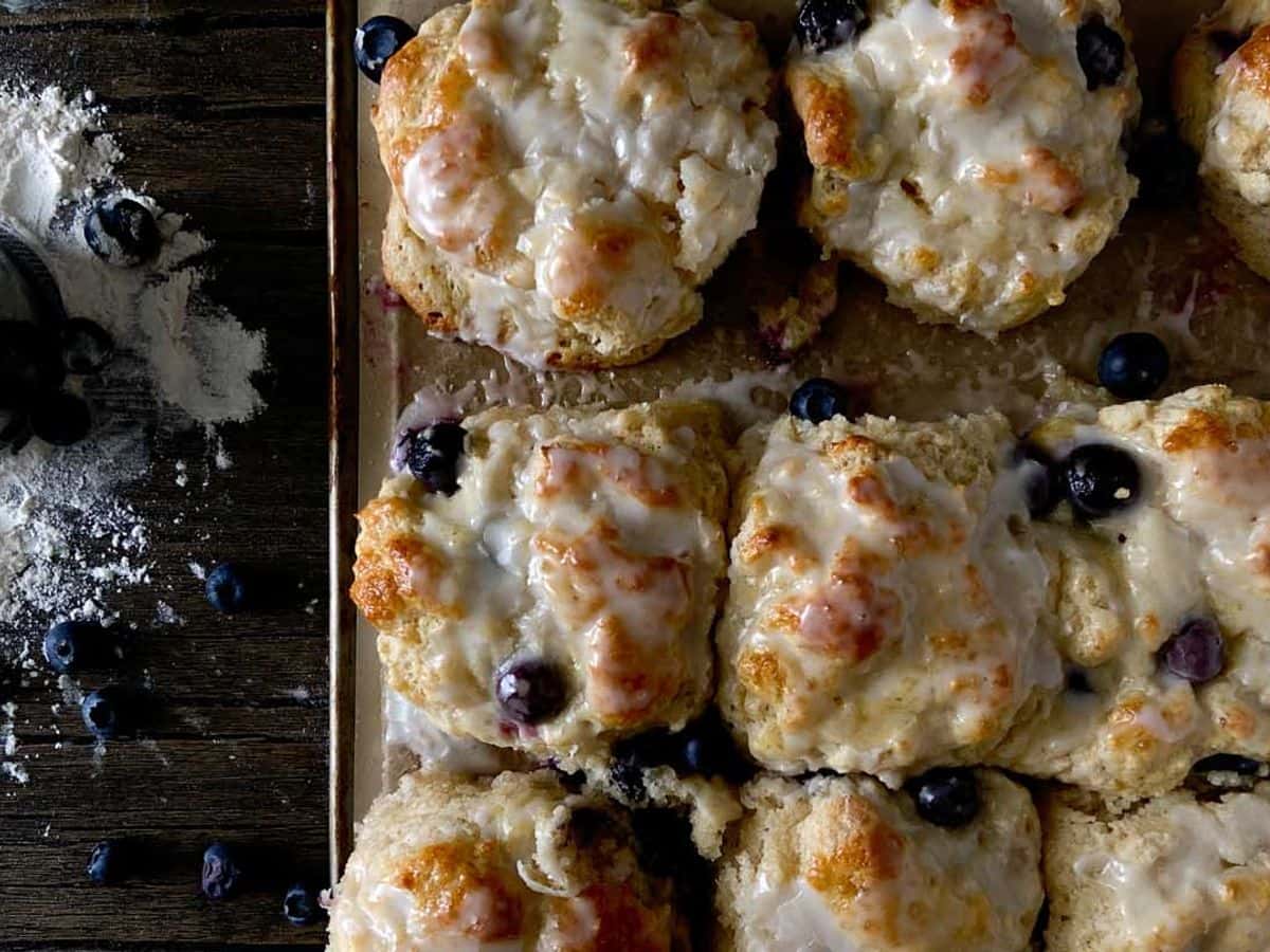 boberry biscuits with blueberries and icing overhead on baking sheet next to biscuit cutter and blueberries