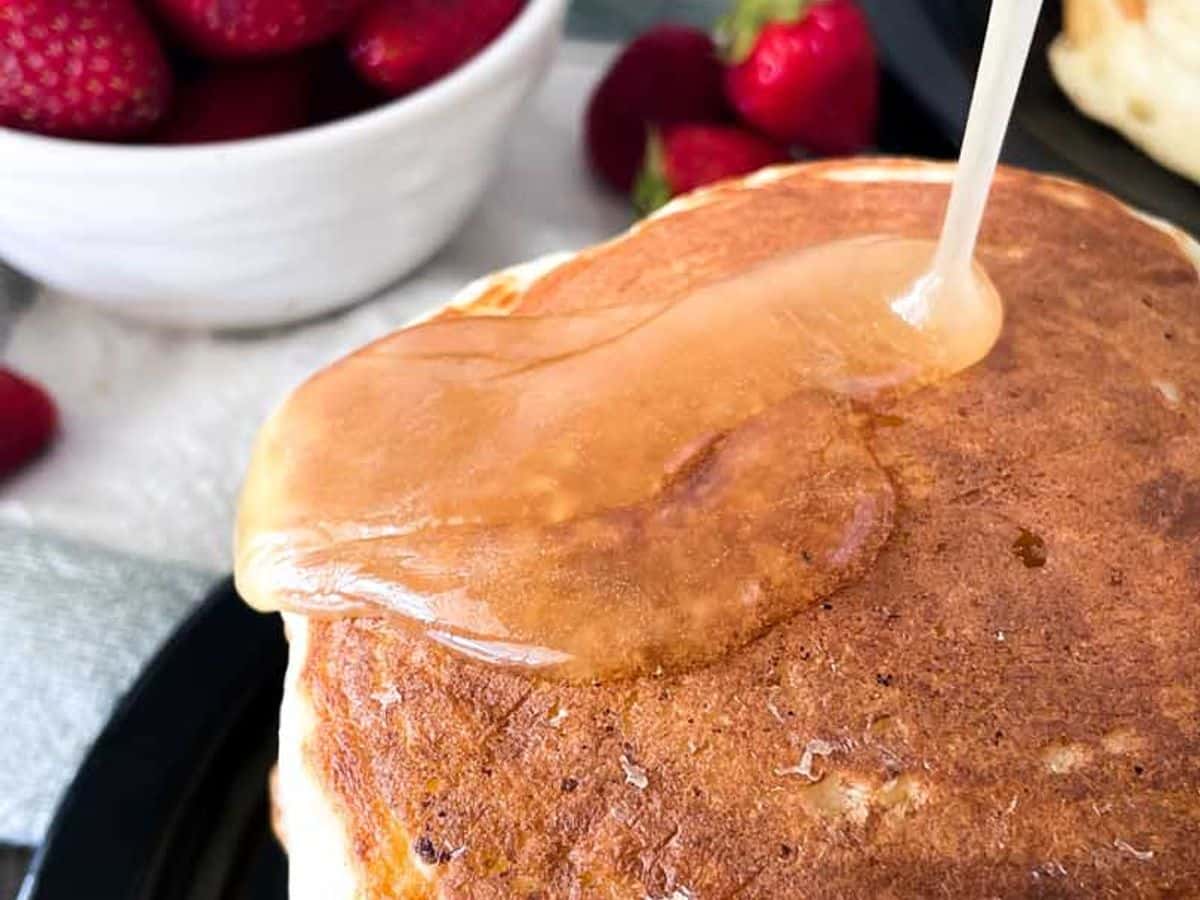 syrup being poured onto a stack of buttermilk pancakes