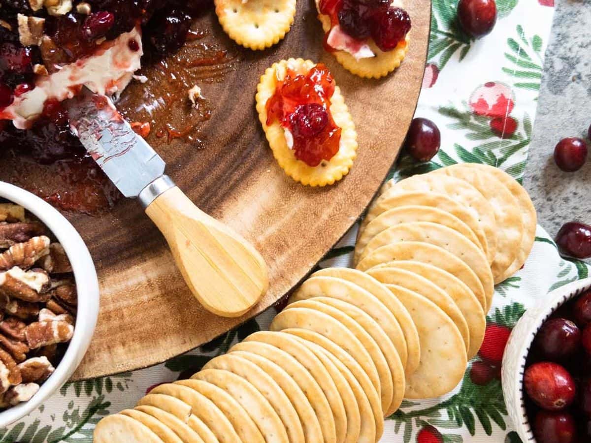 cranberry cream cheese dip on a wood platter with a cheese knife and crackers