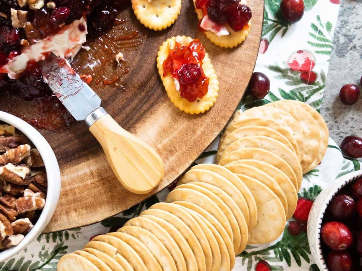 cranberry cream cheese dip on a wood platter with a cheese knife and crackers