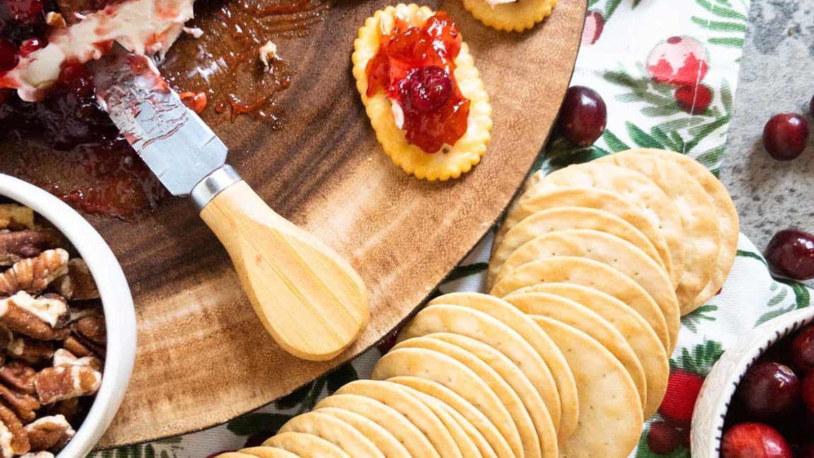 cranberry cream cheese dip on a wood platter with a cheese knife and crackers