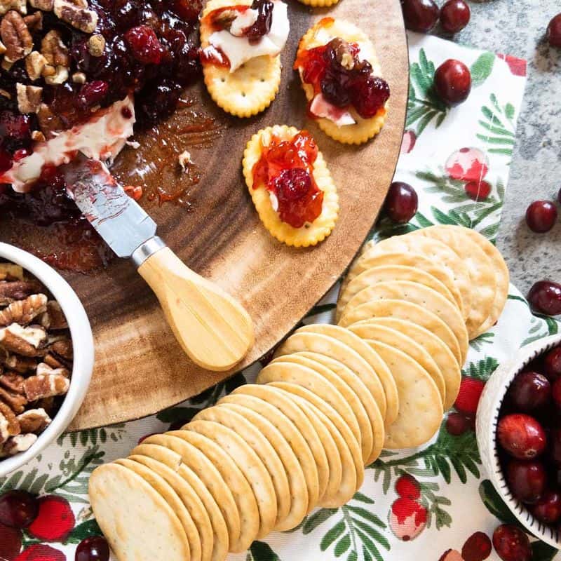 cranberry cream cheese dip on a wood platter with a cheese knife and crackers