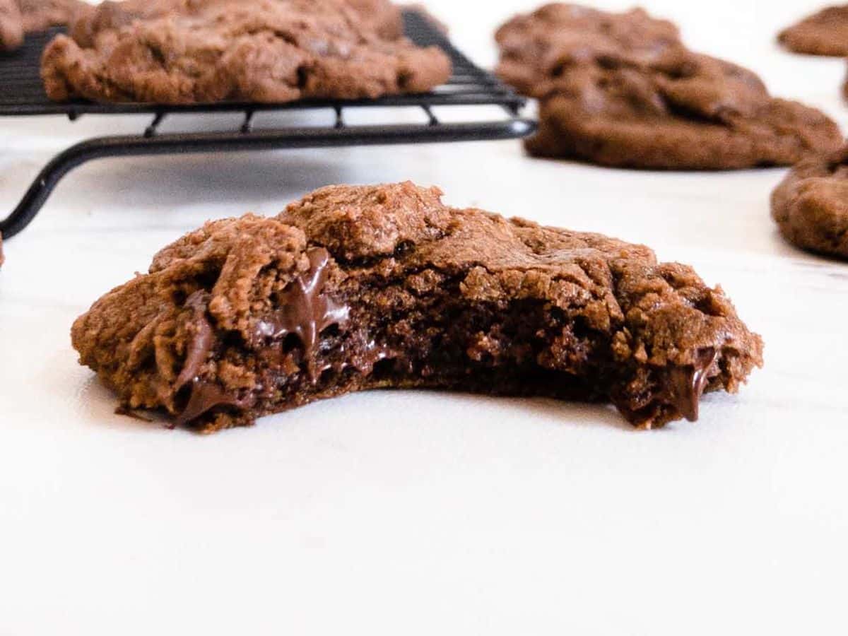 double chocolate chip cookies with a bite taken out of one and others on counter and cooling rack
