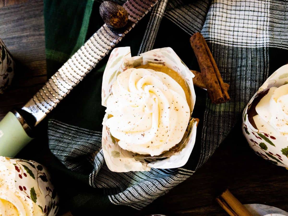 egg nog (tres leches) cupcakes topped with mascarpone and grated nutmeg on counter next to microplane with whole nutmeg and cinnamon sticks