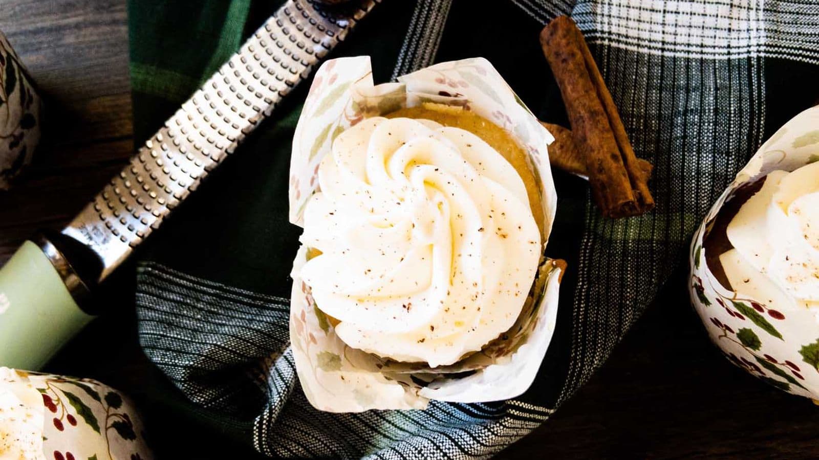 egg nog (tres leches) cupcakes topped with mascarpone and grated nutmeg on counter next to microplane with whole nutmeg and cinnamon sticks