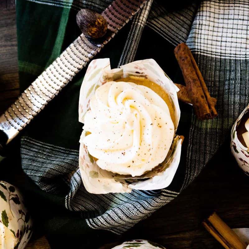 egg nog (tres leches) cupcakes topped with mascarpone and grated nutmeg on counter next to microplane with whole nutmeg and cinnamon sticks