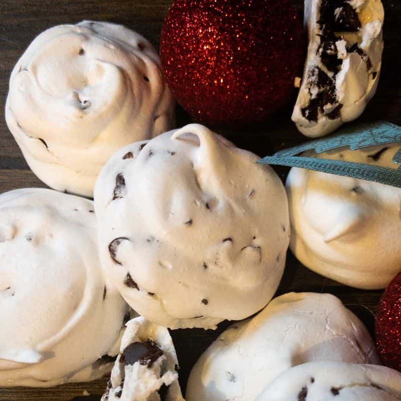 forget me not meringue cookies next to Christmas ornaments and decorations with a few broken to show chocolate chips inside