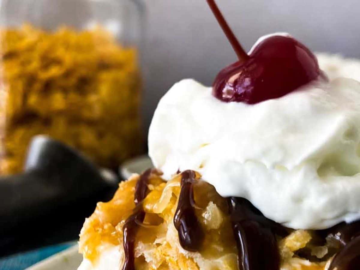 close up of fried ice cream on a plate with chocolate syrup, whipped cream, and a cherry on top