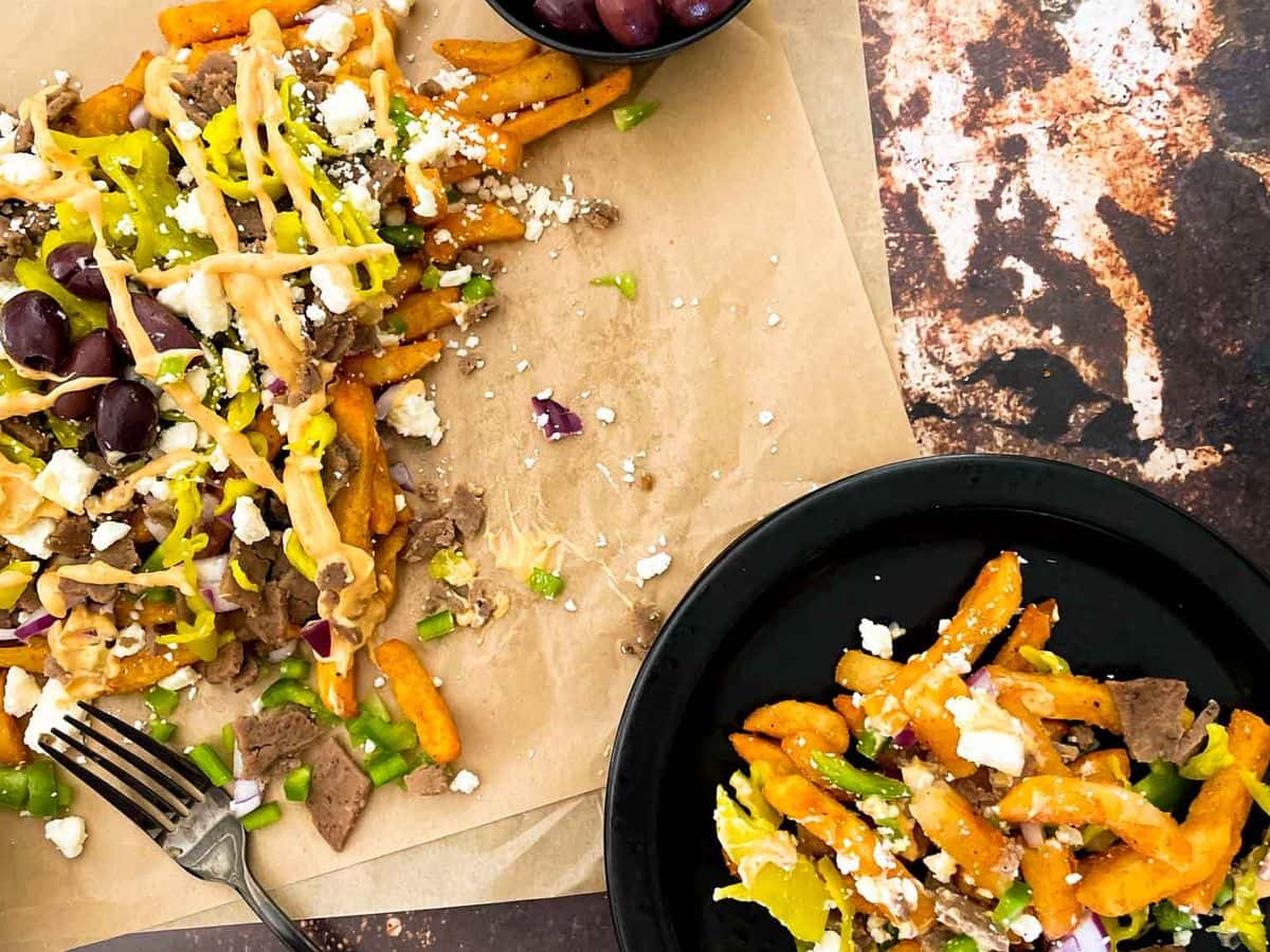 greek street cart fries with gyro doner meat, peppers, onions, olives, pepperoncinis, and aioli sauce, with some on a plate with a fork next to it