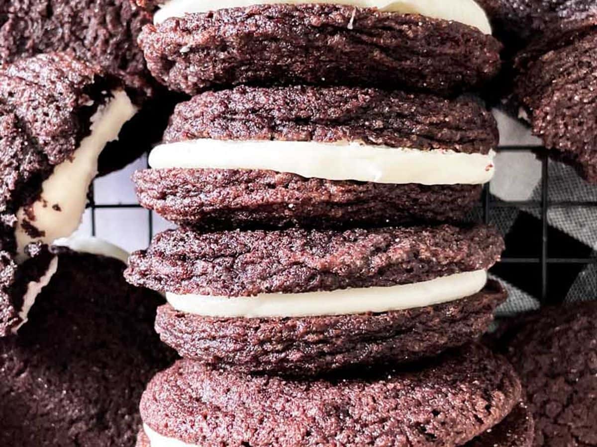 homemade oreo cookies with mascarpone filling lined up next to each other on a cooling rack surrounded by other cookies