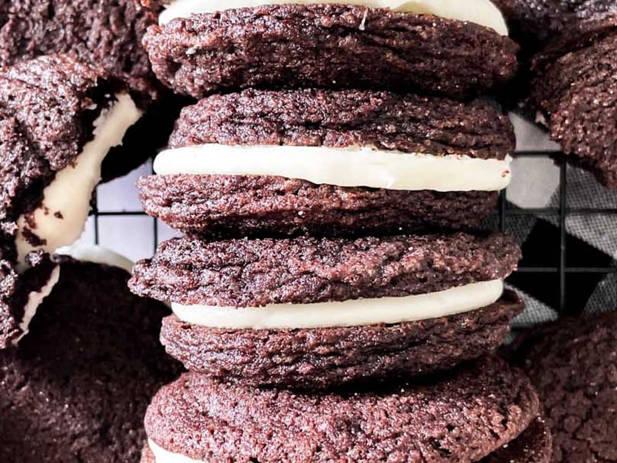 homemade oreo cookies with mascarpone filling lined up next to each other on a cooling rack surrounded by other cookies
