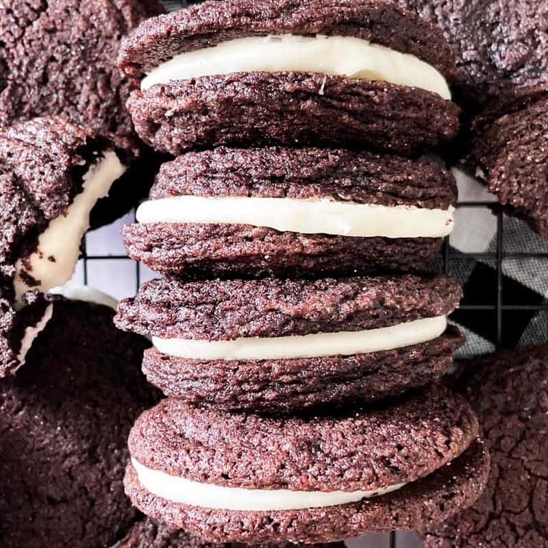 homemade oreo cookies with mascarpone filling lined up next to each other on a cooling rack surrounded by other cookies