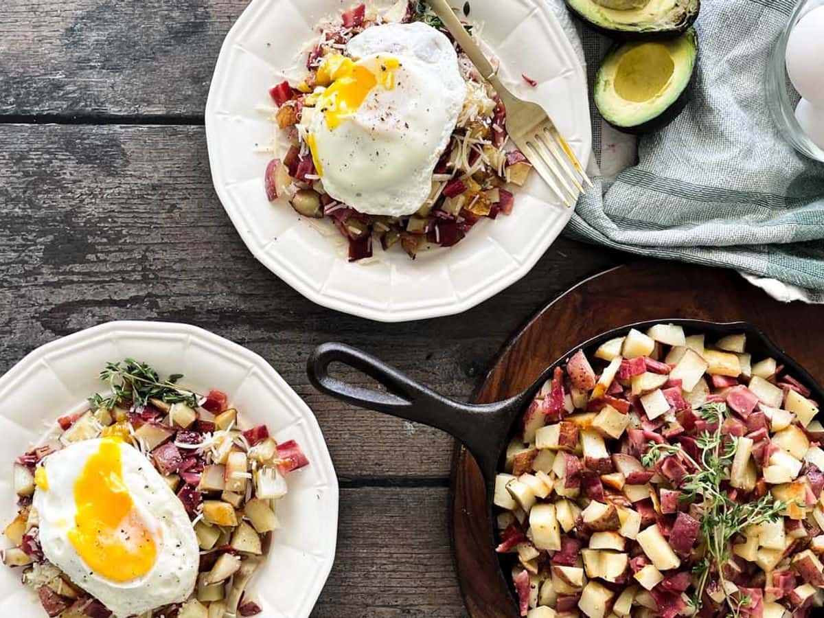 two plates of roasted potatoes and bacon hash topped with parmesan cheese and fried egg next to skillet
