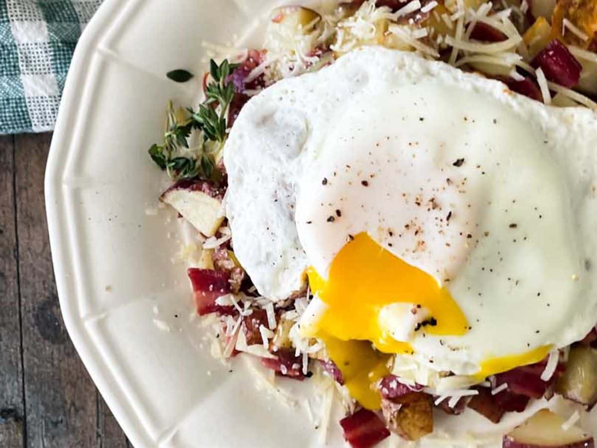 plate of roasted potatoes and bacon hash topped with parmesan cheese and fried egg