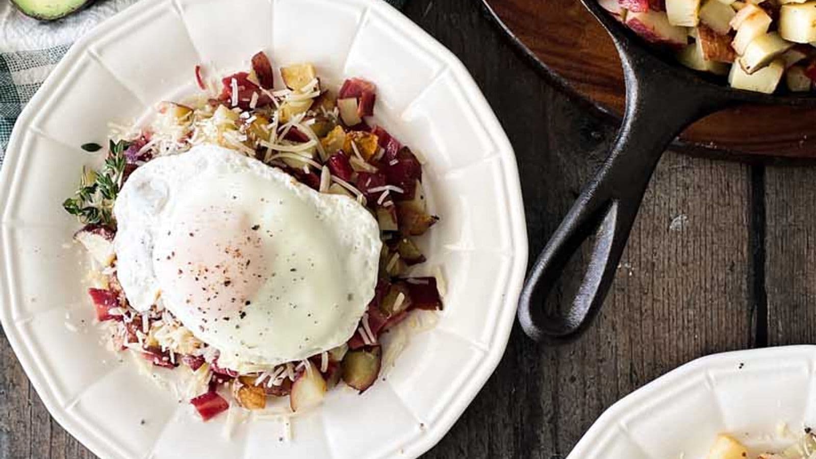 two plates of roasted potatoes and bacon hash topped with parmesan cheese and fried egg surrounded by ingredients