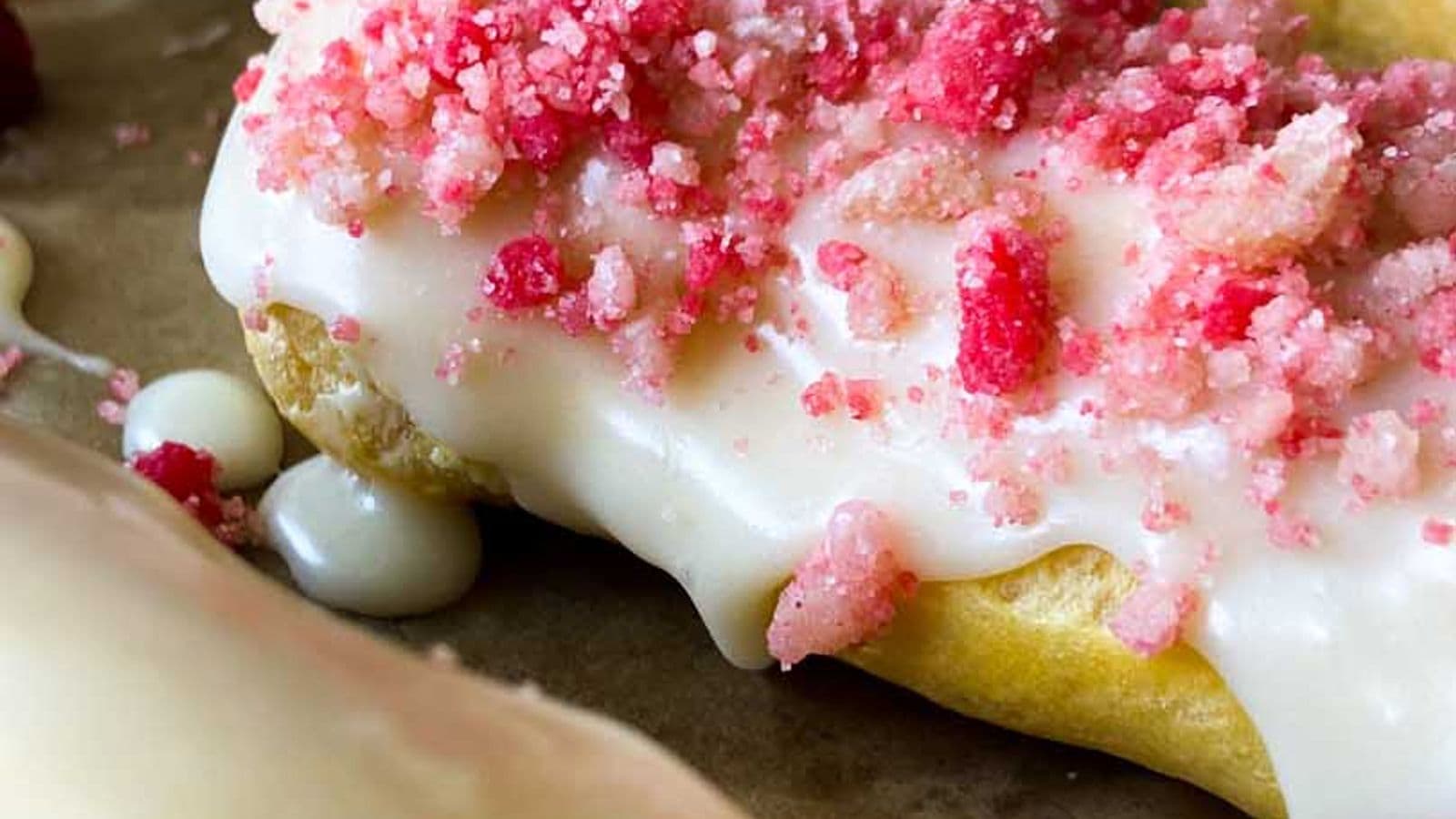 strawberry eclairs finished on baking sheet with glaze and strawberry crunch topping