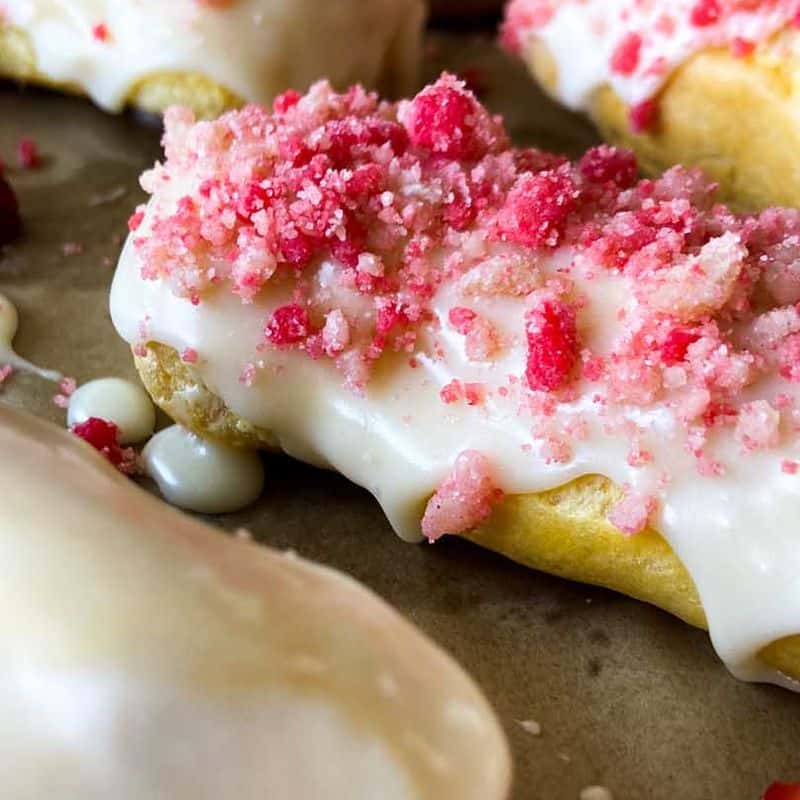 strawberry eclairs finished on baking sheet with glaze and strawberry crunch topping