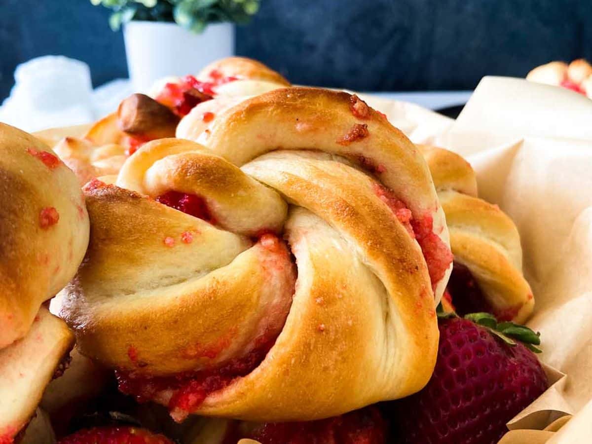 strawberry knot bread rolls in a bowl with flowers in the background