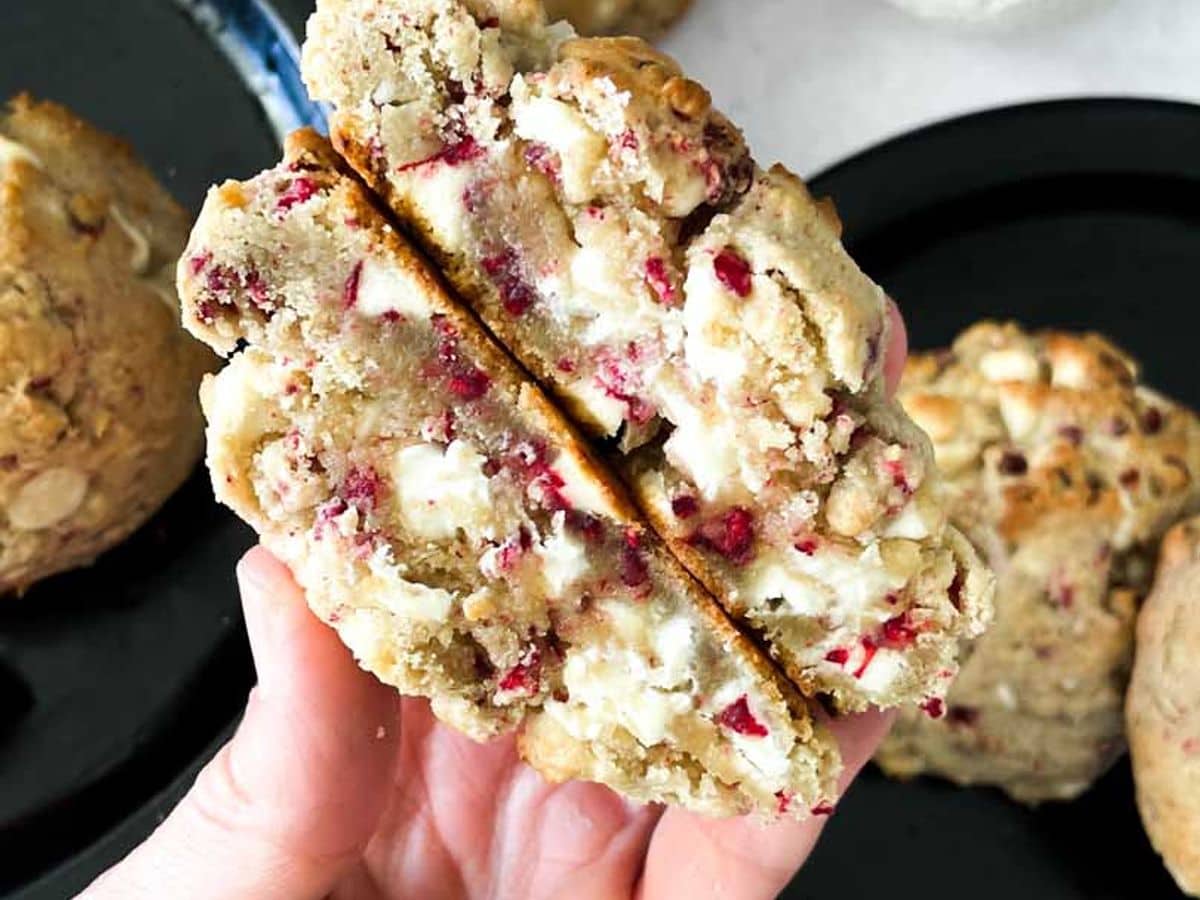 white chocolate raspberry cookie cut in half with both halves held in hand showing inside